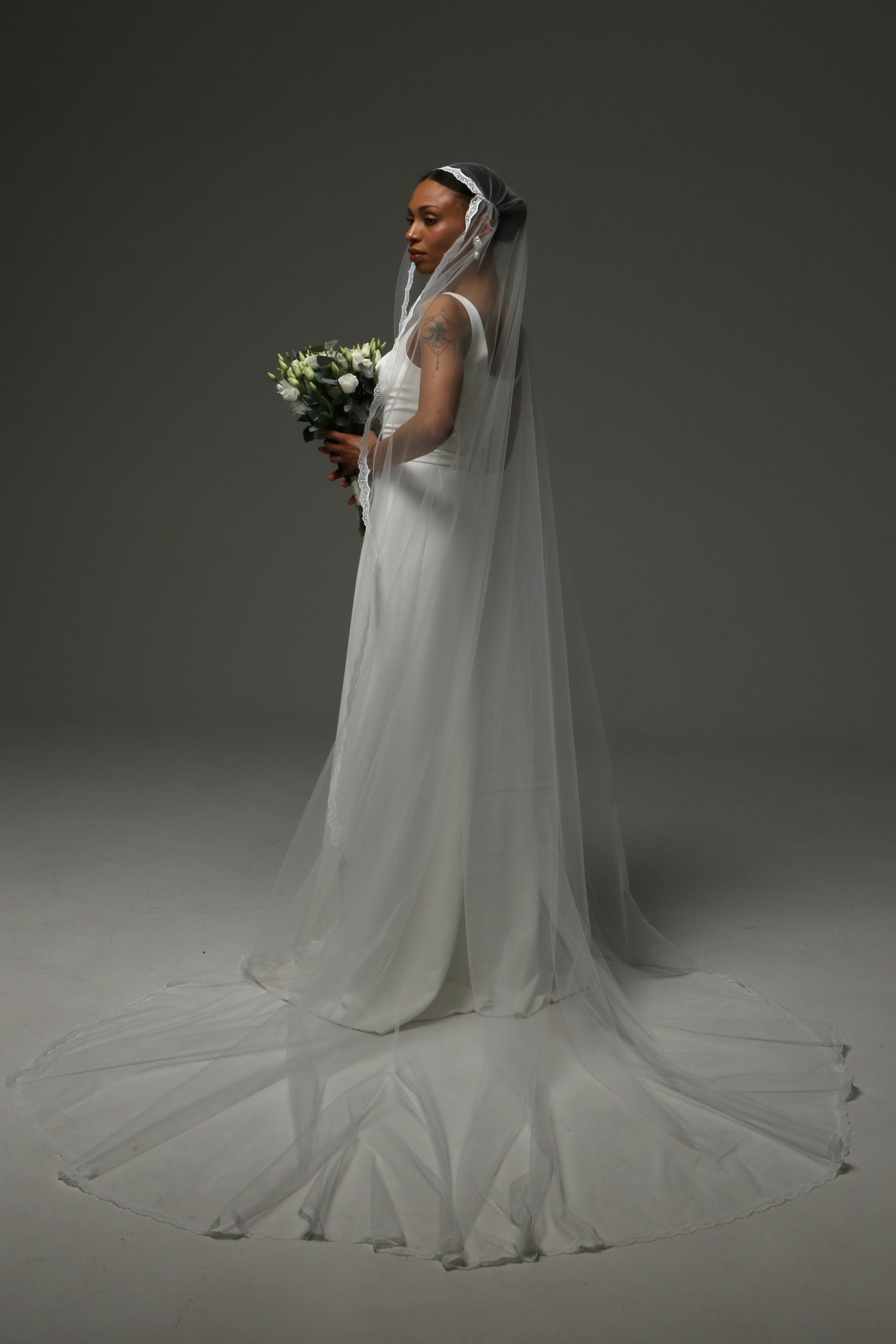 Bride holding a bouquet while wearing a lace-edge cathedral veil.