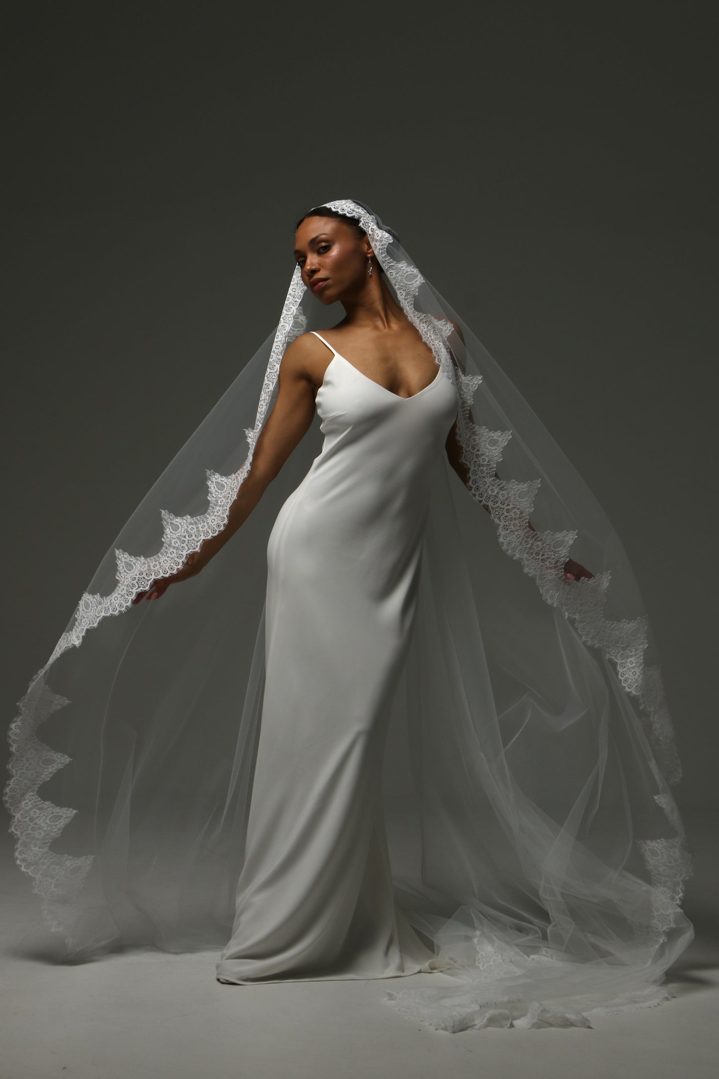 Bride posing in a cathedral mantilla veil with ornate lace detailing.