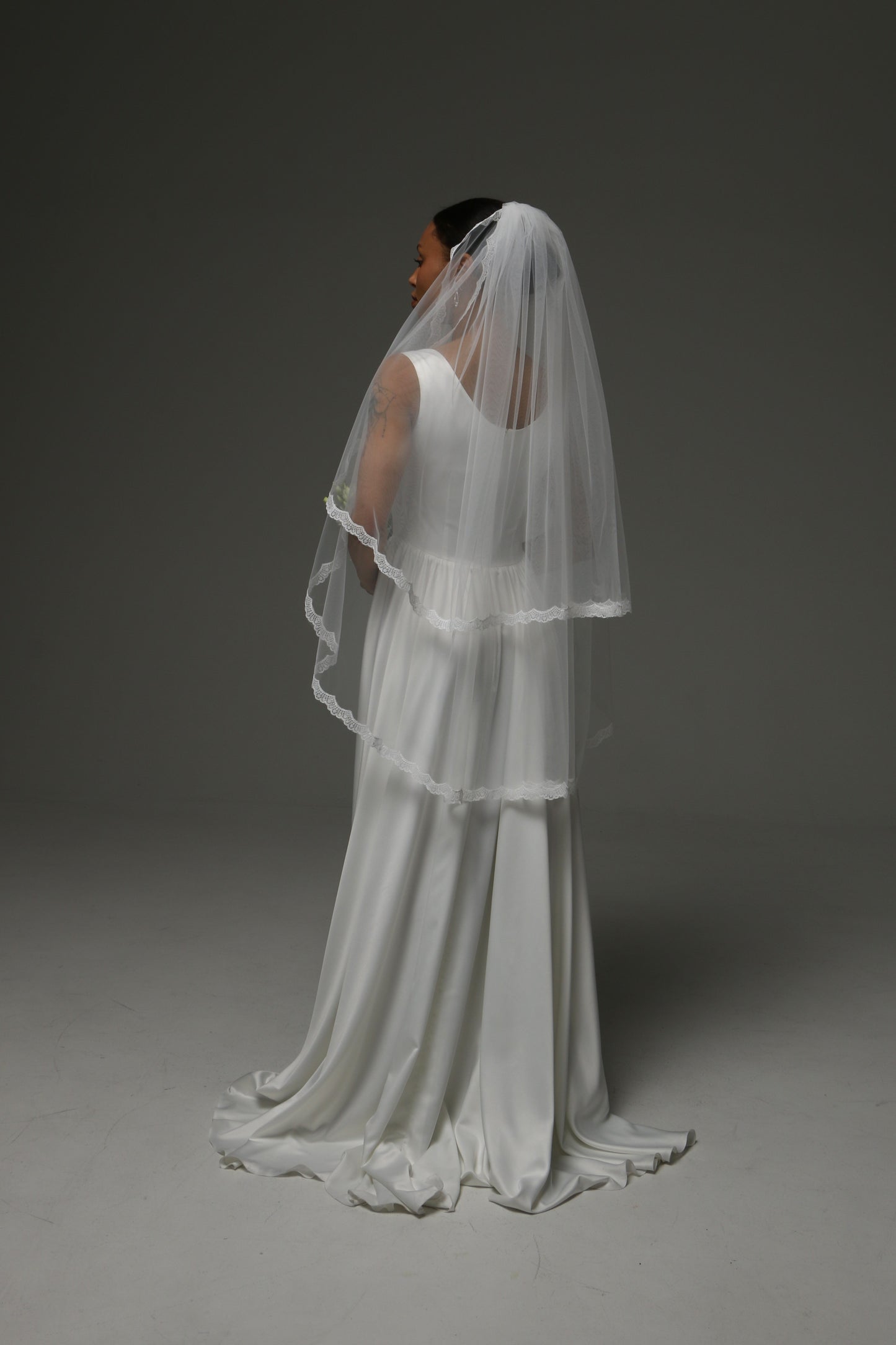 Bride holding a bouquet while wearing a short lace-trimmed veil.