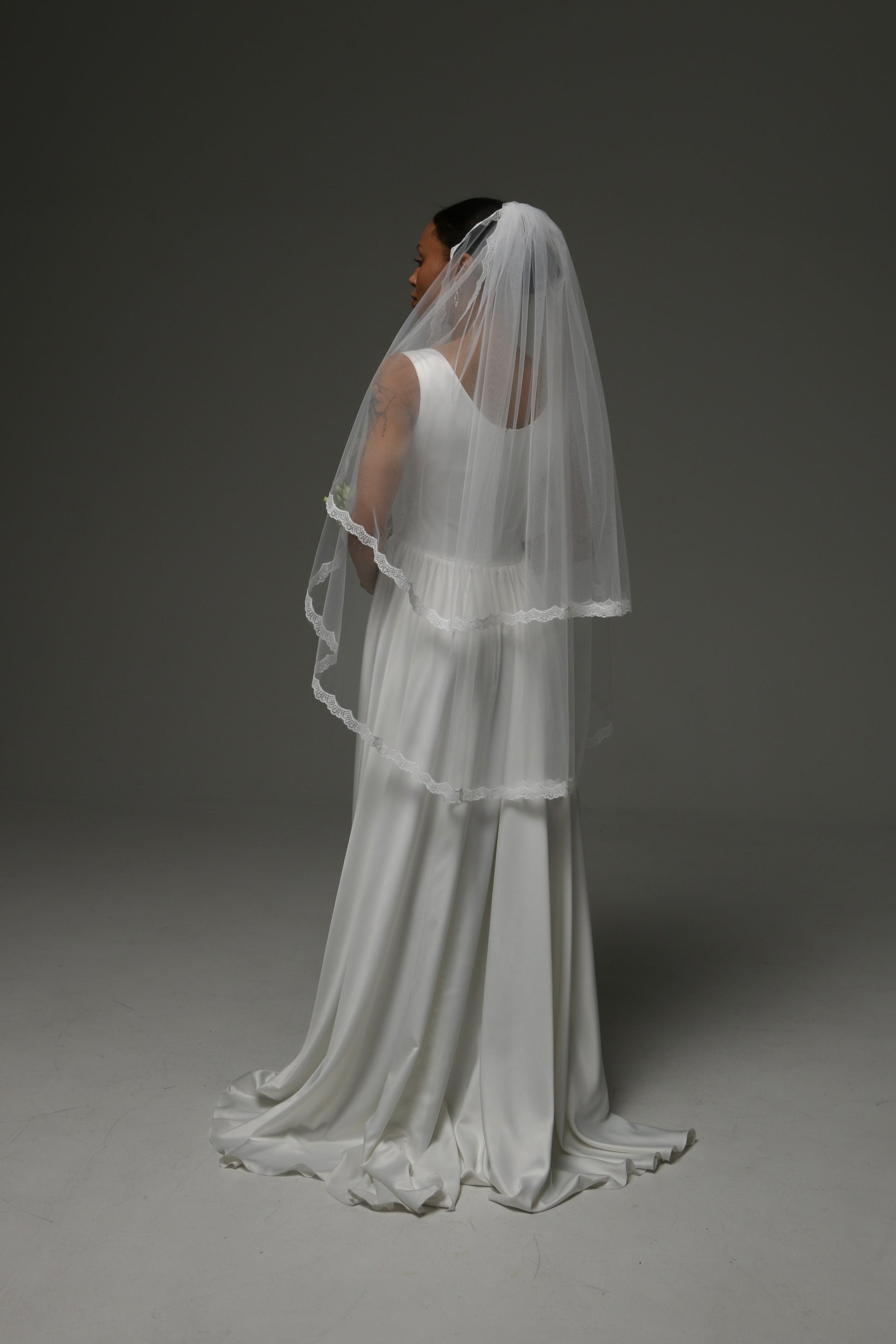 Bride holding a bouquet while wearing a short lace-trimmed veil.