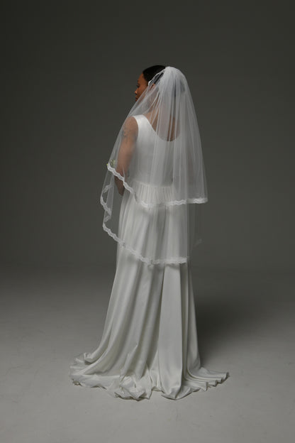 Bride holding a bouquet while wearing a short lace-trimmed veil.