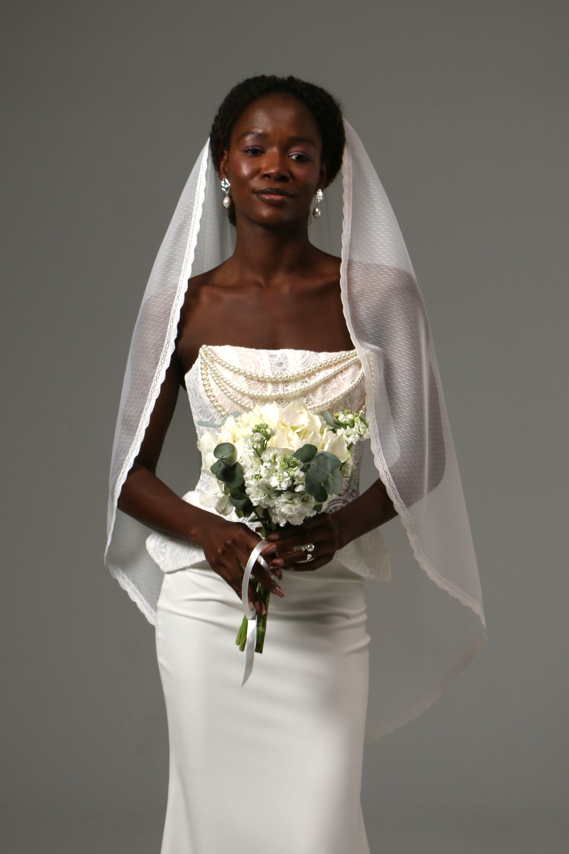 One-tier fingertip wedding veil with dotted tulle and lace edge.