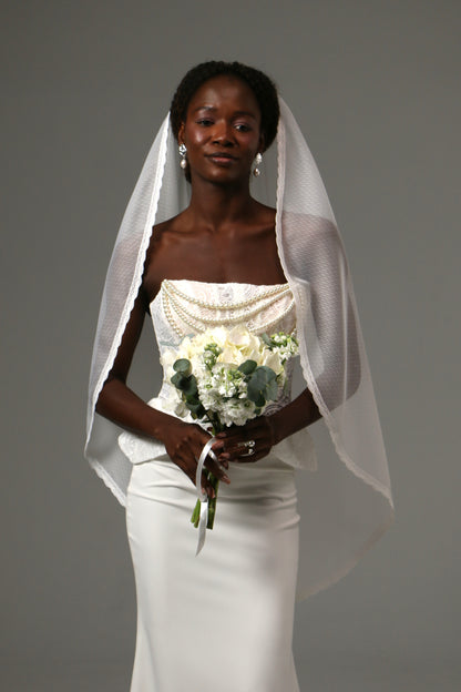 One-tier fingertip wedding veil with dotted tulle and lace edge.