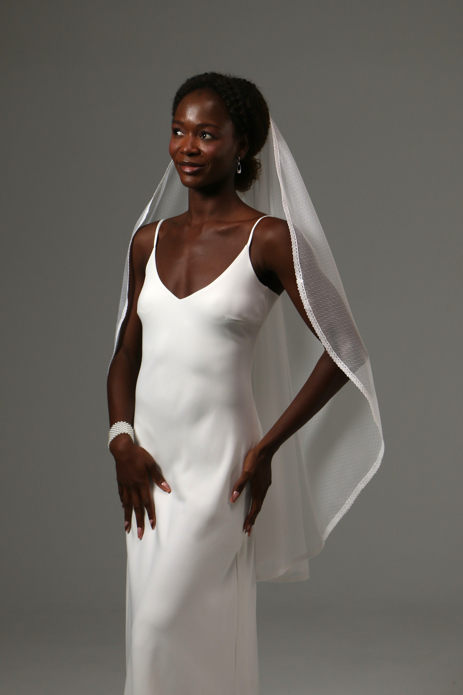 One-tier fingertip wedding veil with dotted tulle and delicate lace edge.