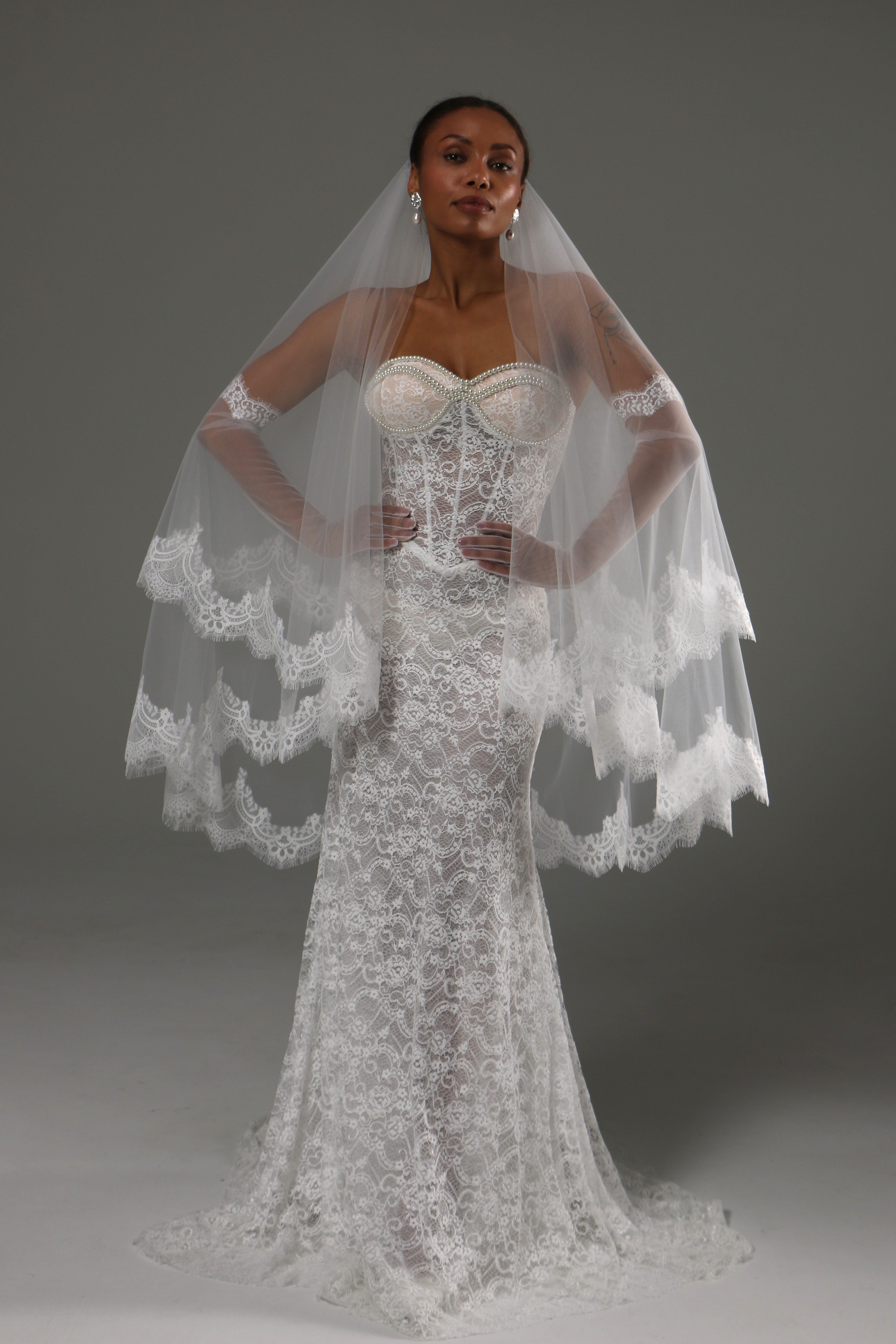 Bride wearing a handmade two-tier cathedral veil with blusher and wide lace edge in a full-length front studio portrait.